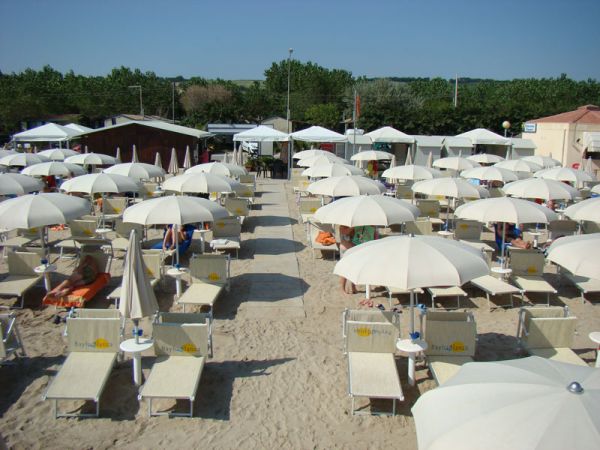 Lettini e ombrelloni bianchi disposti ordinatamente su una spiaggia sabbiosa.