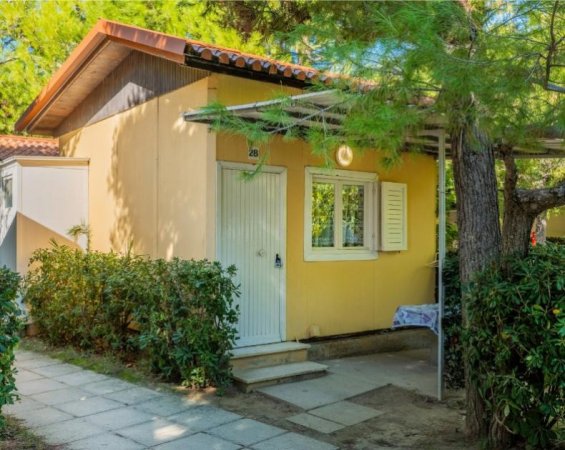 Una casetta gialla con tetto rosso circondata da alberi.