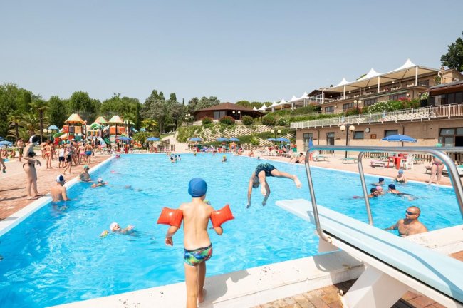 Bambini giocano in piscina, uno con i braccioli arancioni.