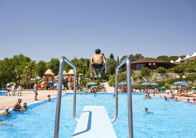 Persona salta dal trampolino in piscina affollata.