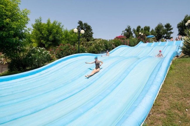 Persone scivolano su acquascivoli blu all'aperto.