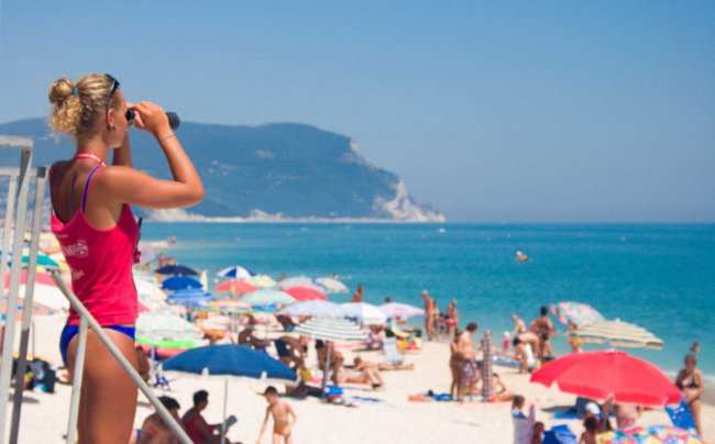Bagnina osserva la spiaggia con binocolo.