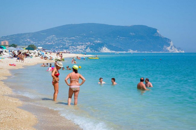 Persone in mare e sulla spiaggia, montagne sullo sfondo.