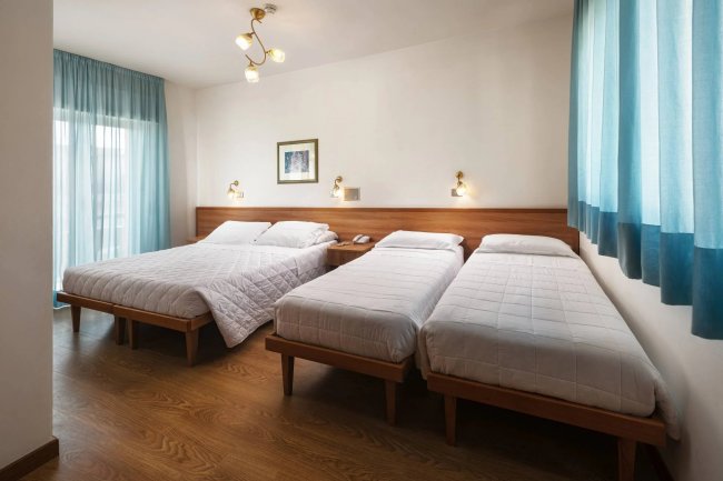 Camera con tre letti, parquet e lampade a parete.