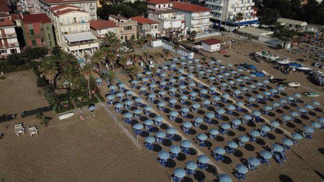 Vista aerea di spiaggia con ombrelloni e edifici.