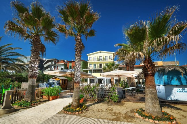 Esterno di un edificio con palme e ombrelloni.