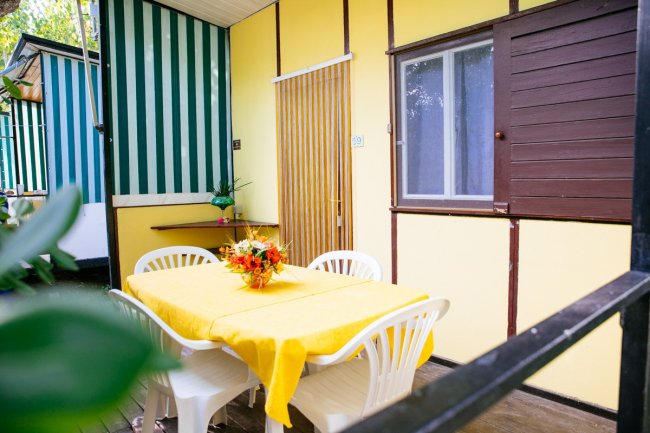 Esterno con tavolo giallo e sedie bianche.