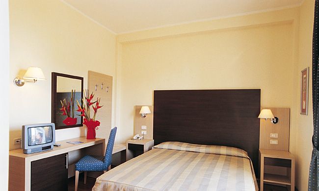 Una camera d'albergo con letto matrimoniale, scrivania, televisore e sedia blu.