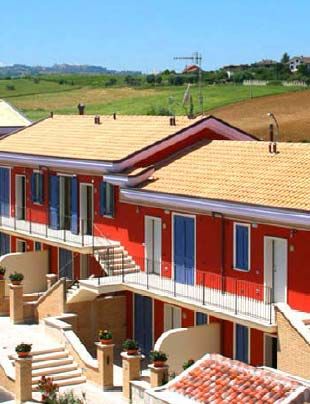 Edificio a due piani di colore rosso con balconi affacciato su paesaggio collinare.
