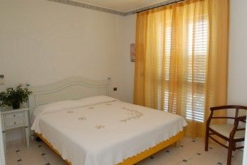 Camera da letto con letto matrimoniale, tende arancioni e sedia di legno.