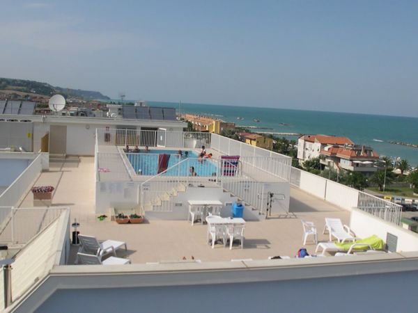 Area sul tetto con piscina, sedie a sdraio e vista sul mare.