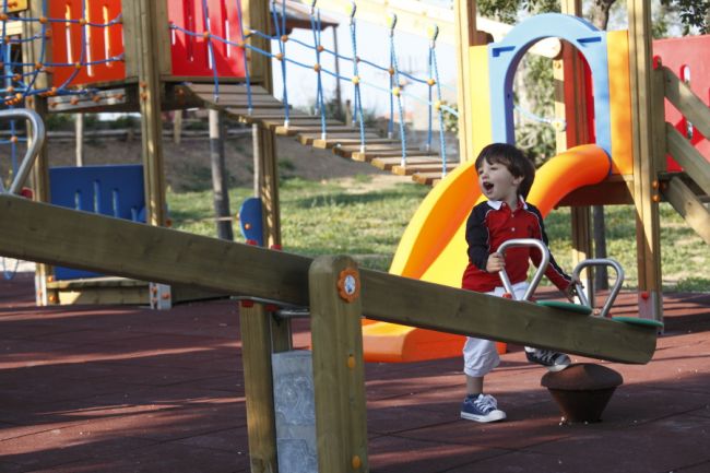 Un bambino gioca sorridente su un'altalena in un parco giochi colorato.