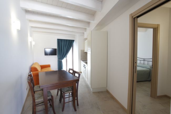 Sala con divano arancione, tavolo da pranzo, TV a parete e ingresso in una camera da letto.