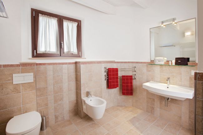 Bagno moderno con piastrelle beige, lavabo, bidet e due asciugamani rossi.