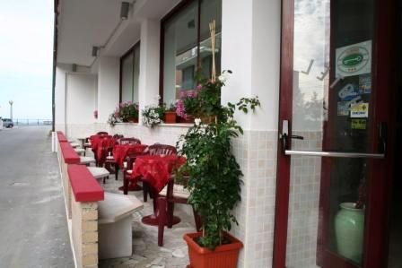Area esterna con tavoli e sedie rosse, e fioriere con piante davanti a una finestra.