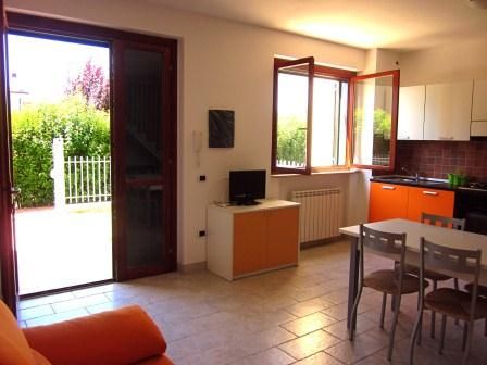 Soggiorno con divano arancione, tavolo da pranzo, cucina moderna, e porta aperta verso il giardino.