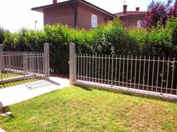 Giardino verde con siepi e recinzione metallica.