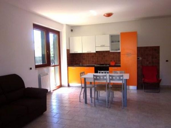 Cucina moderna con mobili arancioni, tavolo bianco e sedie grigie.