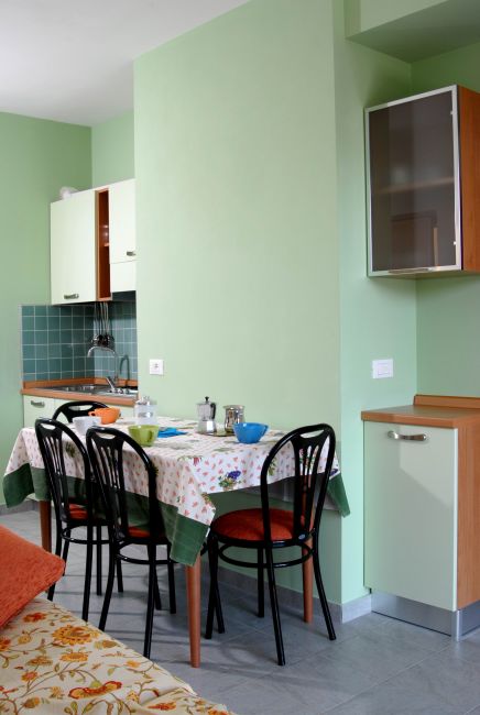 Tavolo da pranzo con tovaglia a fiori e sedie nere, cucina sullo sfondo.