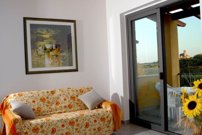 Salotto con divano fiorito, quadro di girasoli e porta finestra su un balcone.