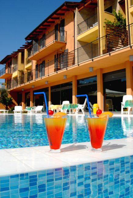 Due cocktail arancioni con cannucce blu su bordo piscina, hotel sullo sfondo.