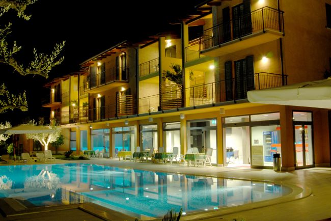 Hotel illuminato di notte con piscina e lettini all'aperto.